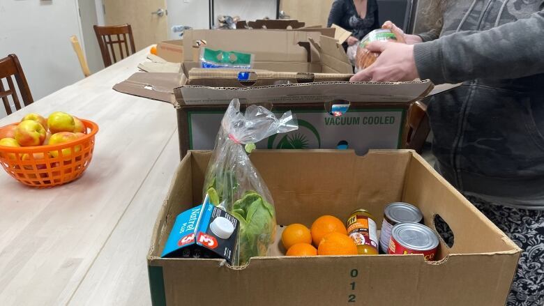 Boxes of food are lined up on a table, with someone's hands visible putting something in a box.