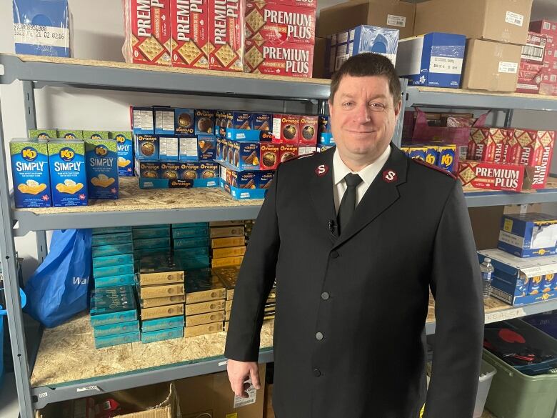 A man in a Salvation Army jacket stands in front of a shelf of food.