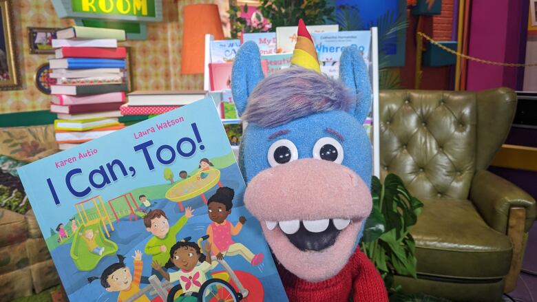 A unicorn puppet holds up a children's picture book, smiling.