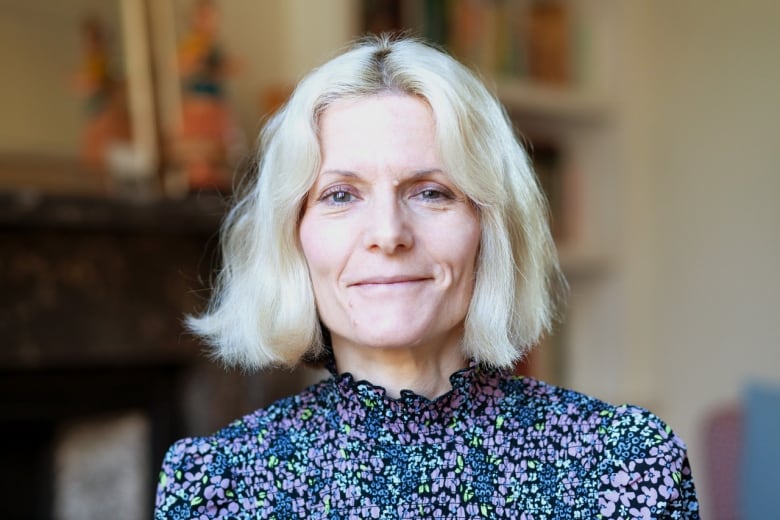 Close up of a woman with short blonde hair wearing a blue-green floral top.