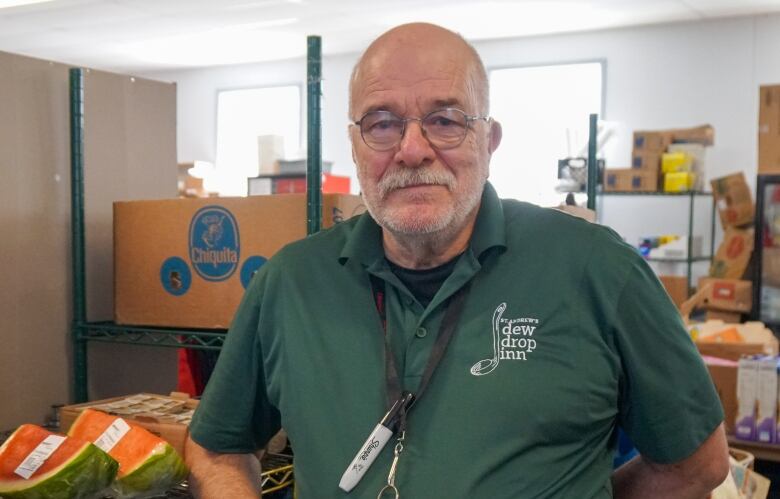 A man wearing glasses and a green shirt stands in front of boxes of food.