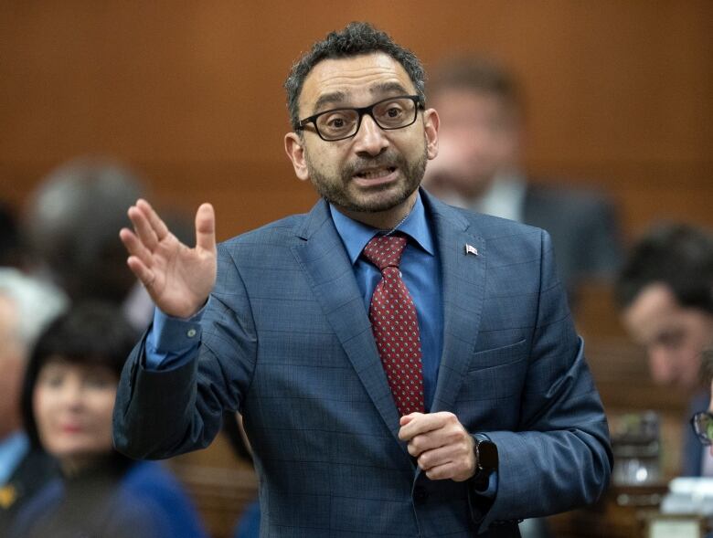 A man in a suit gestures while speaking. 