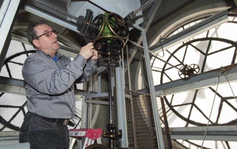 A man adjusts the gears on a giant clock inside the clock tower of a fire hall. 