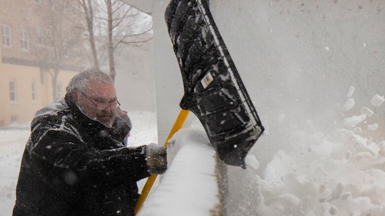 A man is picture shoveling snow atop a snow bank.