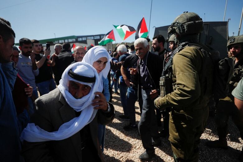 Soldiers and protesters gathered outside, some people holding Palestinian flags.