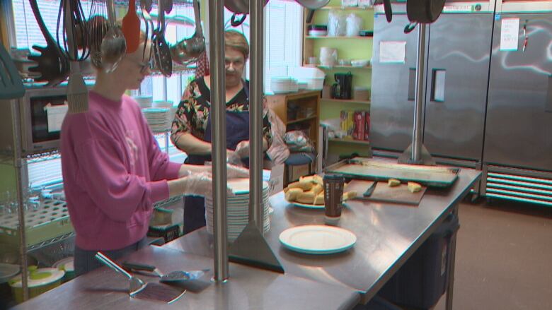 Two women prepare food at a stainless steel counter.