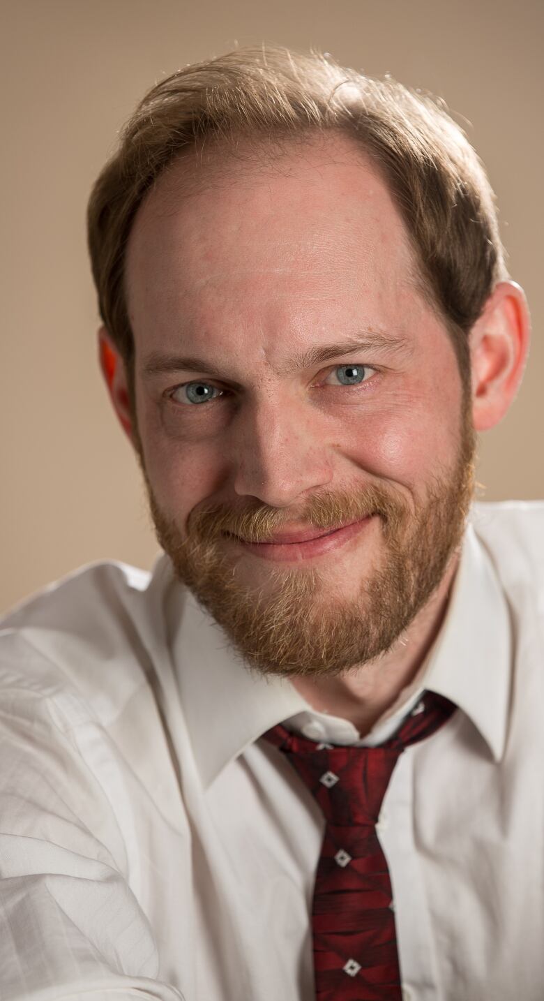 A smiling, bearded man in a white dress shirt and tie.