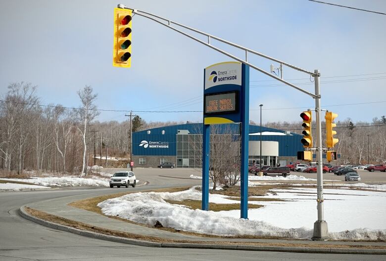 A building with a blue facade and large windows is shown from a distance across the street, with a large electronic sign out front saying Emera Centre Northside.