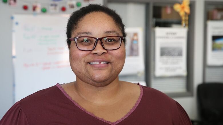 A smiling woman in a red shirt stands in an office. 