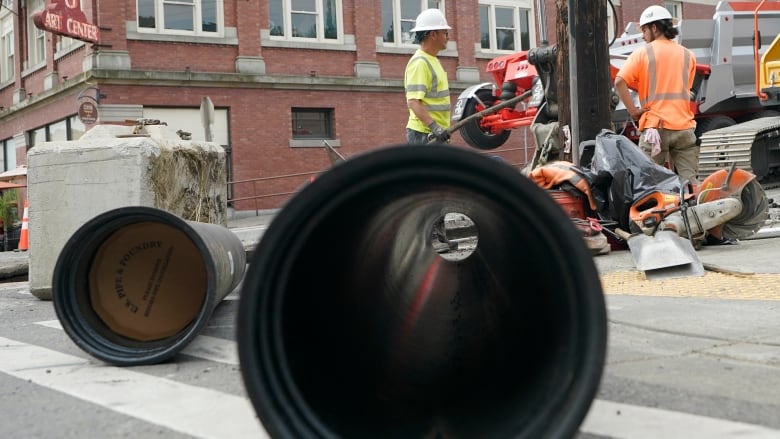 Big water pipes sit on the road as workers install them in the background. 