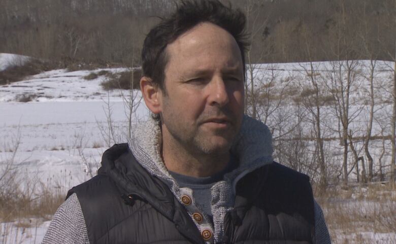 A man with short brown hair stands outside.