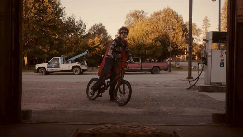 A boy on a bike wearing a ninja turtle mask. 