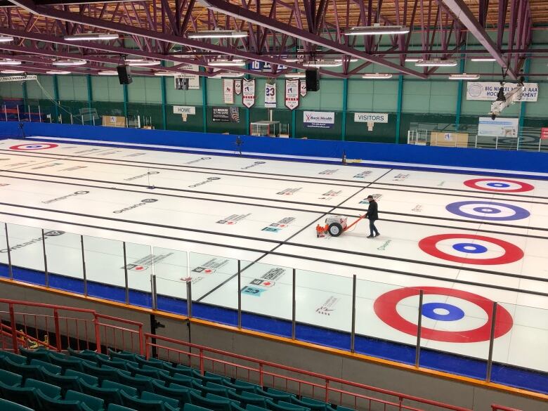 A man pushing a small machine on a large ice surface with four curling rinks painted.