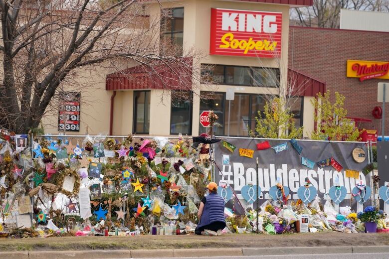 Exterior of a grocery store with a fence covered in flowers and tributes including a sign that reads Boulder Strong