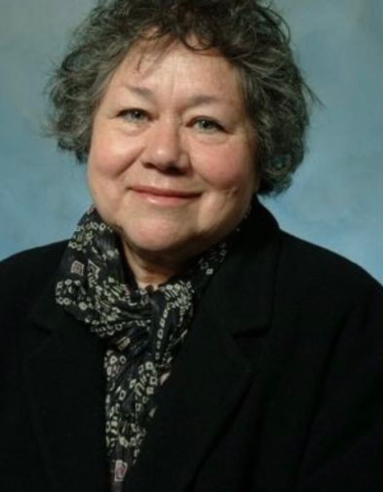 A smiling woman wearing a black shirt and a scarf sits in front of a blue background.