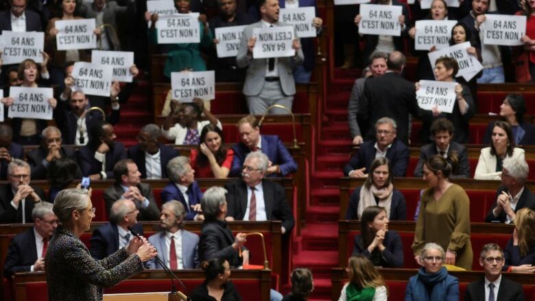 French parliamentarians stand holding signs to protest against a government bill on pension reforms.