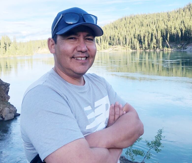 A smiling man stands beside a river. 