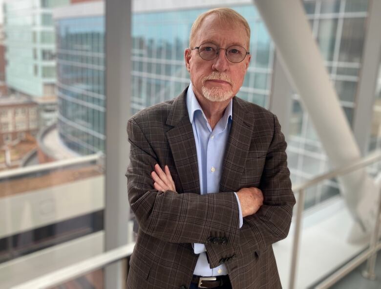 A man with glasses and a goatee stands with his arms crossed.