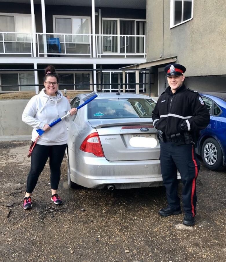 A woman and a police officer in uniform pose in front of a vehicle. 