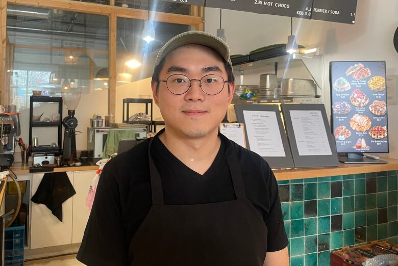 A man in a black shirt and hat stands in front of a restaurant counter.