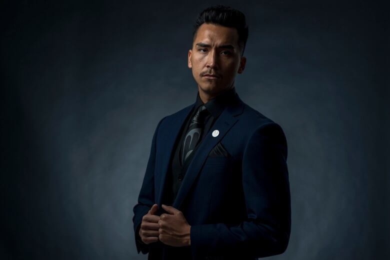 An Indigenous man wearing a suit poses for a professional protrait.