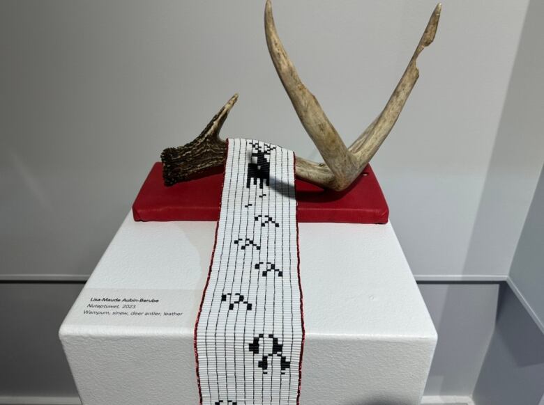 A long, white strip of fabric with an embroidered deer and deer tracks rests on a deer antler.