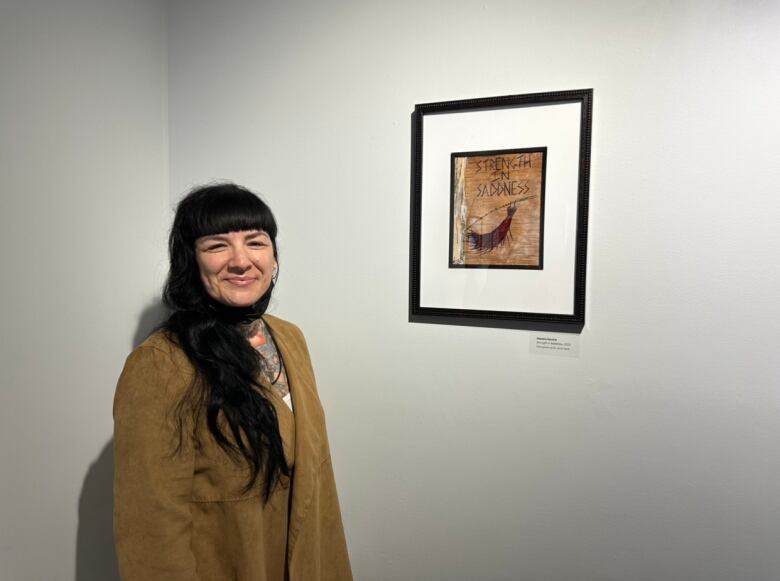 A woman with long black hair stands next to a piece of art made using birch bark.