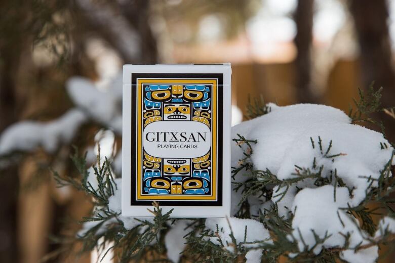 A box that says Gitxsan playing cards sits on a snowy branch