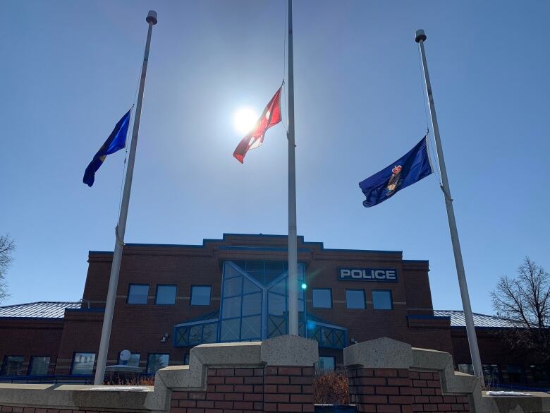 Three poles with lowered flagsin front of a brick and glass building, illuminated by the sun. 