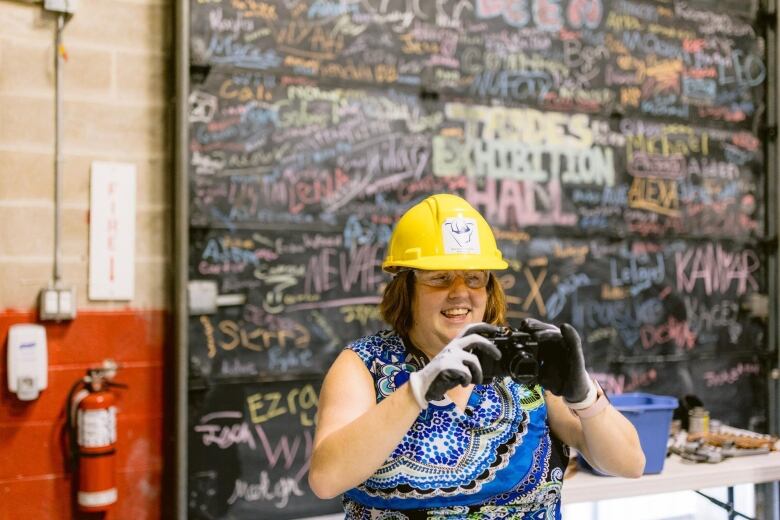 A woman with a hard hat holds up a camera.