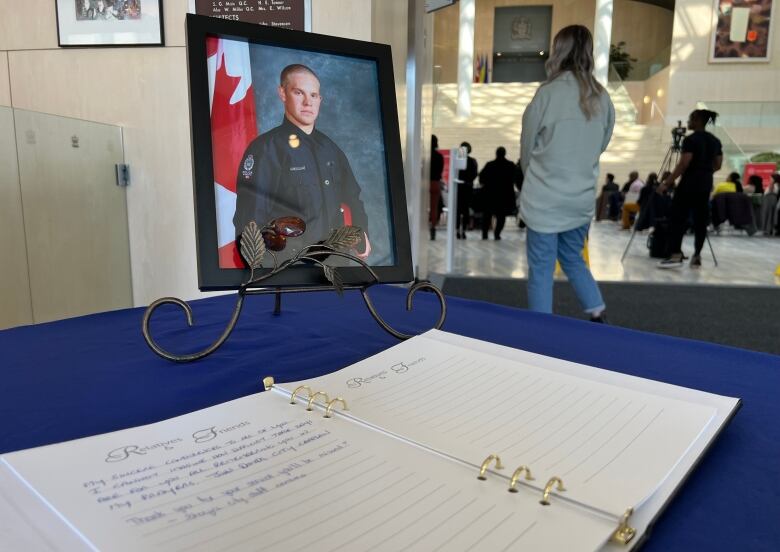 A framed portrait of a man stands behind a book on a table draped with a blue cloth. 