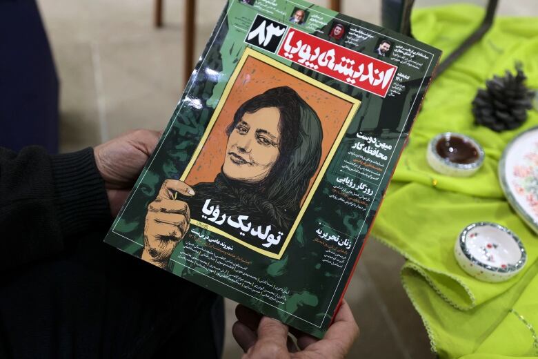 A magazine cover featuring an illustration of a young woman in a headscarf is shown in the hands of someone reading it while seated at a table.