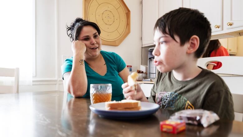 A mother sits at the kitchen table with her son to ensure he doesn't eat his food to fast. 