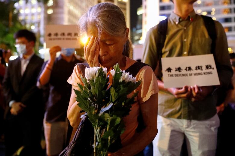 An elderly woman holding flowers covers her eye as she attends a protest in Hong Kong, China August 30, 2019. 