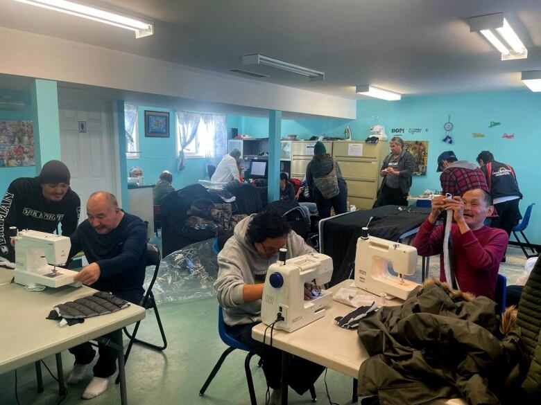 A room full of men bending over sewing machines.