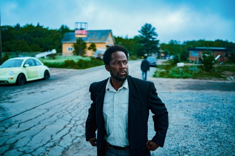 A man wearing a suit stands on the road of a rundown town.