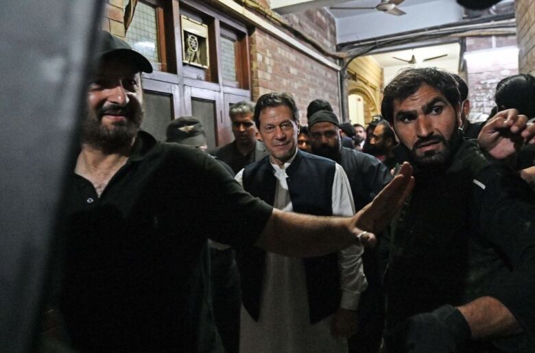 Security personnel guard a man, centre, and use a bullet proof shield to protect him.