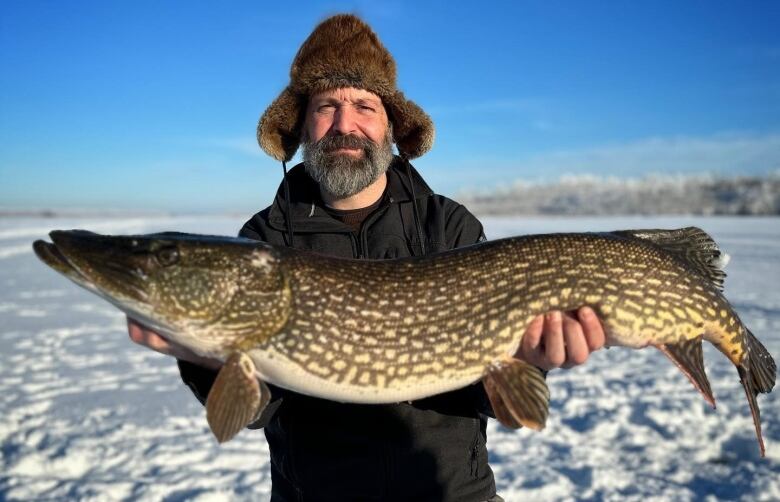 A man standing on a snow-covered frozen lake holds up a large fish.