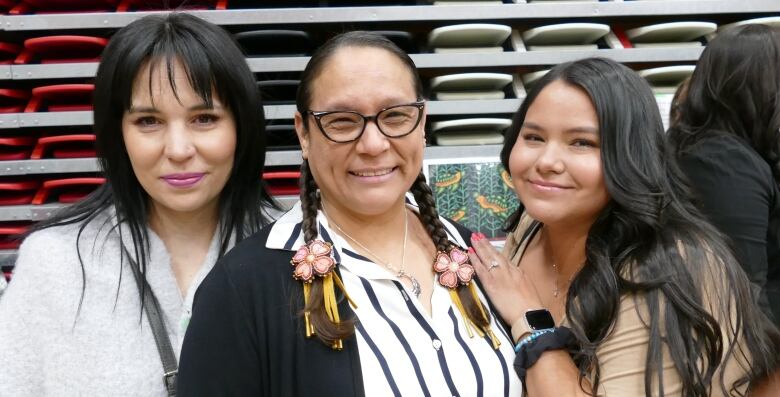 Three women are standing shoulder to shoulder, smiling and looking at the camera.