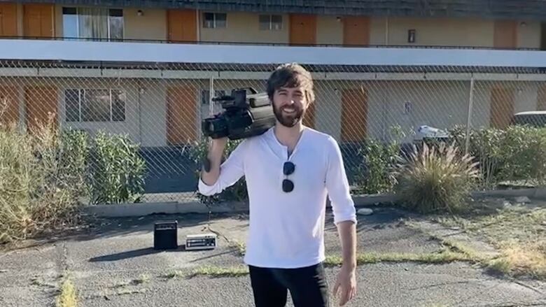 A man smiling at the camera in a sunny day. He's holding a video camera.