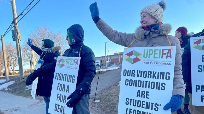 People with signs that say 'fighting for a fair deal' and 'our working conditions are students' learning conditions' stand on the sidewalk at UPEI.