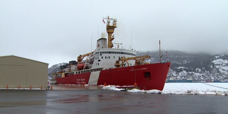 A large red and white boat floats in ice-covered water.