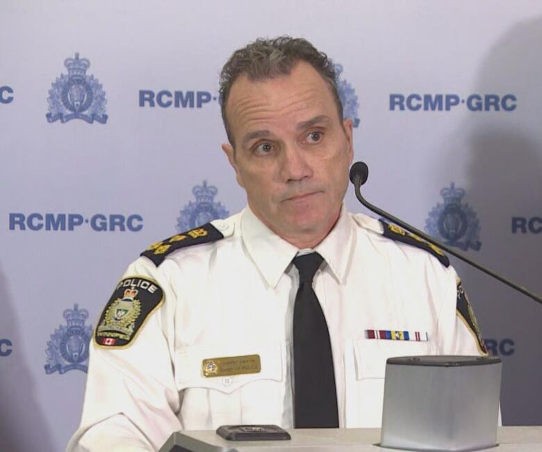 A police officer in a white shirt speaks into a microphone at a podium