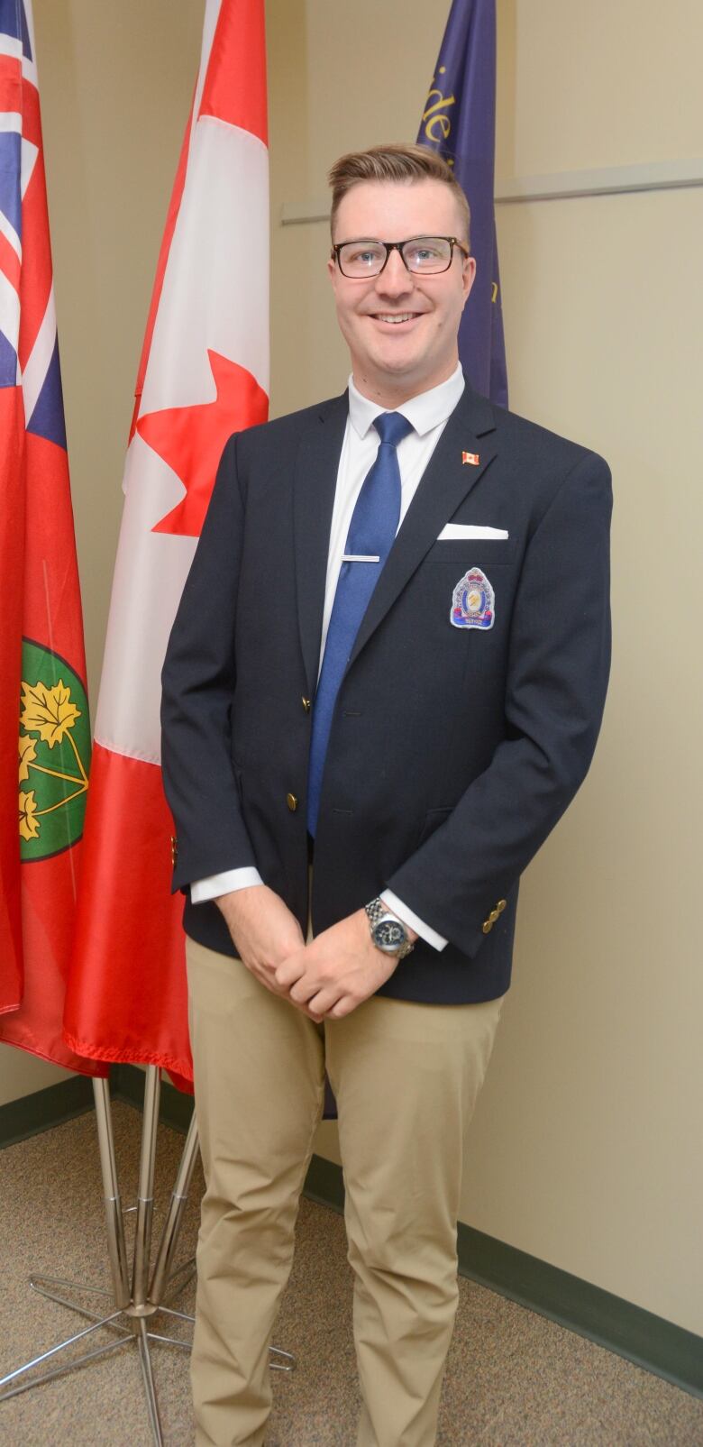 A smiling man wearing a suit with a Canadian and Ontario flag in the background.