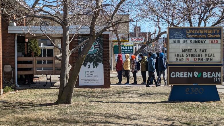 Students line up outside a church. There's a sign outside advertising a free meal.