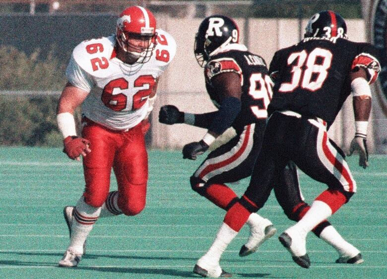 A man in a Calgary Stampeders uniform charges forward on a football field.