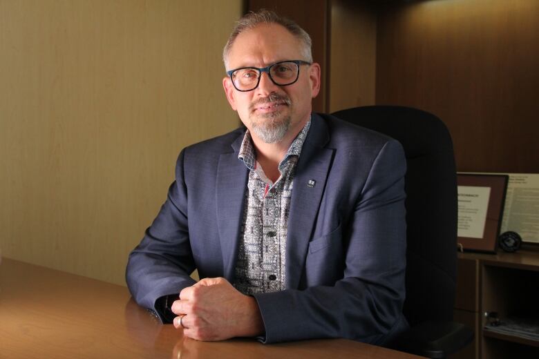 A man, Steinbach Mayor Earl Funk, sits forward on a chair, leaning forward toward the desk.