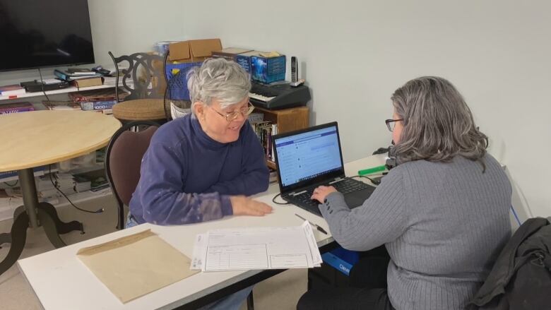 A man and a woman sitting across a table from each other. The woman is working on a computer. 