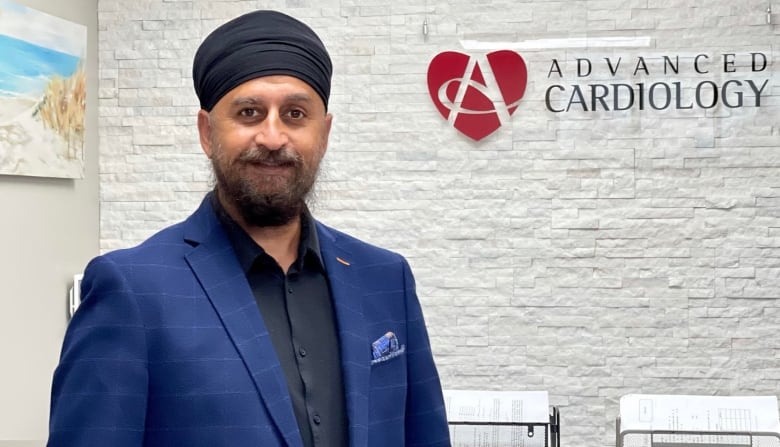 Dr. Anmol Kapoor stands in front of a sign in his clinic, that reads Advanced Cardiology.