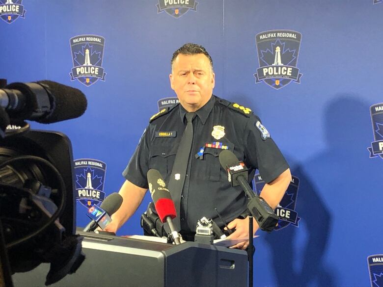 A police officer stands behind a podium with several microphones attached to it.